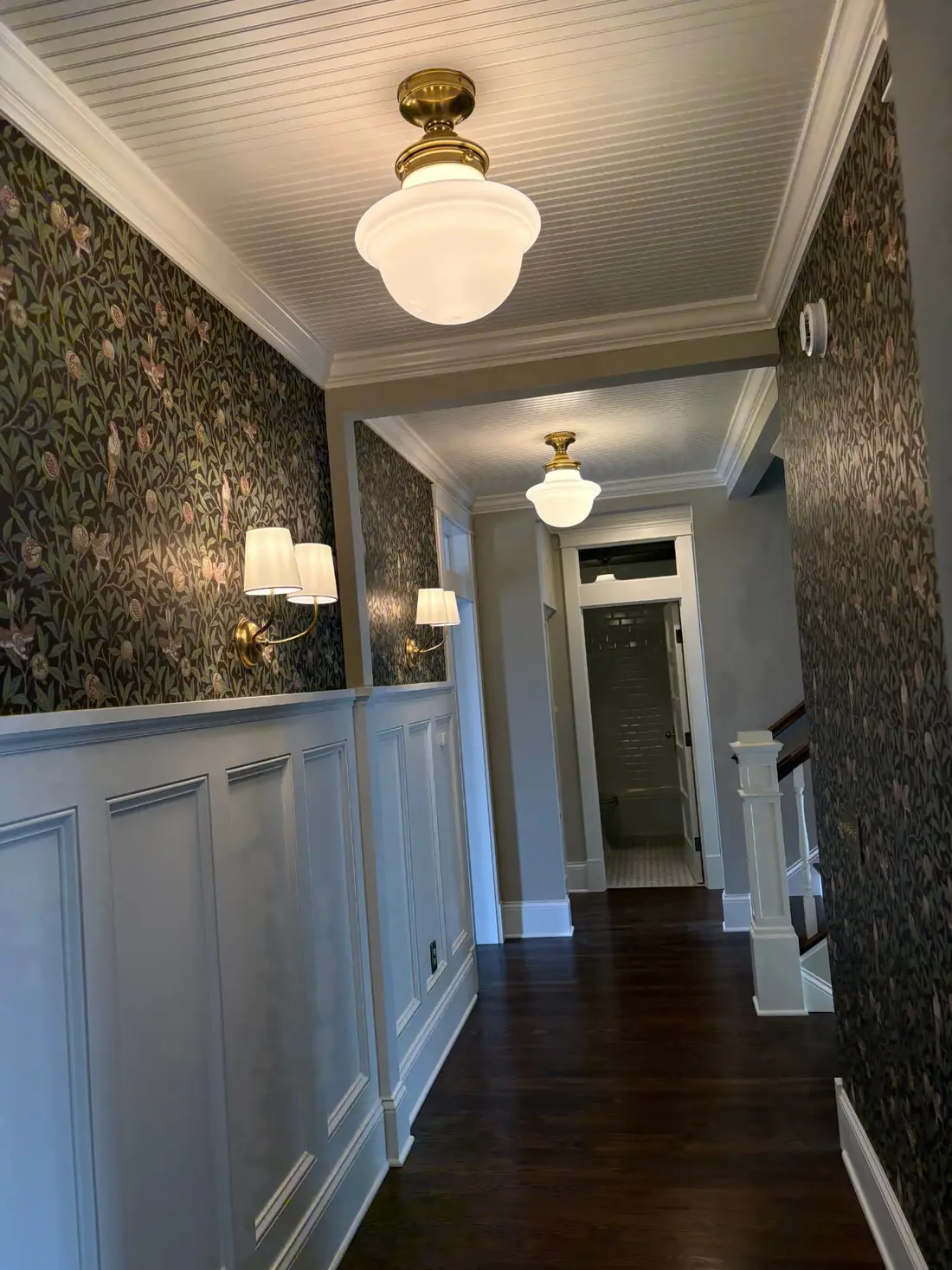 Elegant interior hallway with custom wainscoting, wall sconces, and brass ceiling fixtures